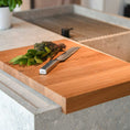 Bild in Galerie-Betrachter laden, Hackbrett aus Eichenholz, Antirutschkante, hochkant 34 x 50 x 3,5 cm, rechts unten Logo von COOKX eingraviert, Milieubild in Küche, Brett liegt auf Kücheninsel, Kräuter und silbernes Messer auf Brett