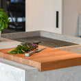 Bild in Galerie-Betrachter laden, Hackbrett aus Eichenholz, Antirutschkante, hochkant 34 x 50 x 3,5 cm, rechts unten Logo von COOKX eingraviert, Milieubild in Küche, Brett liegt auf Kücheninsel, Kräuter und silbernes Messer auf Brett