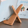 Bild in Galerie-Betrachter laden, Buchständer in X-Form aus naturfarbener Eiche, minimalistisches Design mit geschwungenen Haken-Enden, Milieubild mit Buch drauf