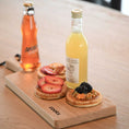 Bild in Galerie-Betrachter laden, Servierbrett oder Schneidebrett aus Eichenholz Natur mit Griff und schwarzem Lederband zum aufhängen, 400mmx180mmx25mm, Milieubild im Esszimmer auf Tisch, Brett mit Essen und Getränken drauf