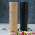 Bild in Galerie-Betrachter laden, Salz-/Pfeffermühle Set, eins aus Eichenholz schwarz und eins aus Eichenholz Natur, 23cm hoch, Milieubild in Küche, Set steht hinter Teller mit Salat. Frontalansicht