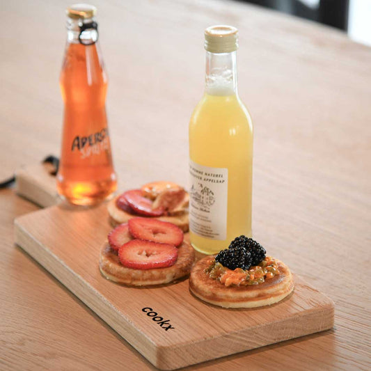 Servierbrett oder Schneidebrett aus Eichenholz Natur mit Griff und schwarzem Lederband zum aufhängen, 400mmx180mmx25mm, Milieubild im Esszimmer auf Tisch, Brett mit Essen und Getränken drauf