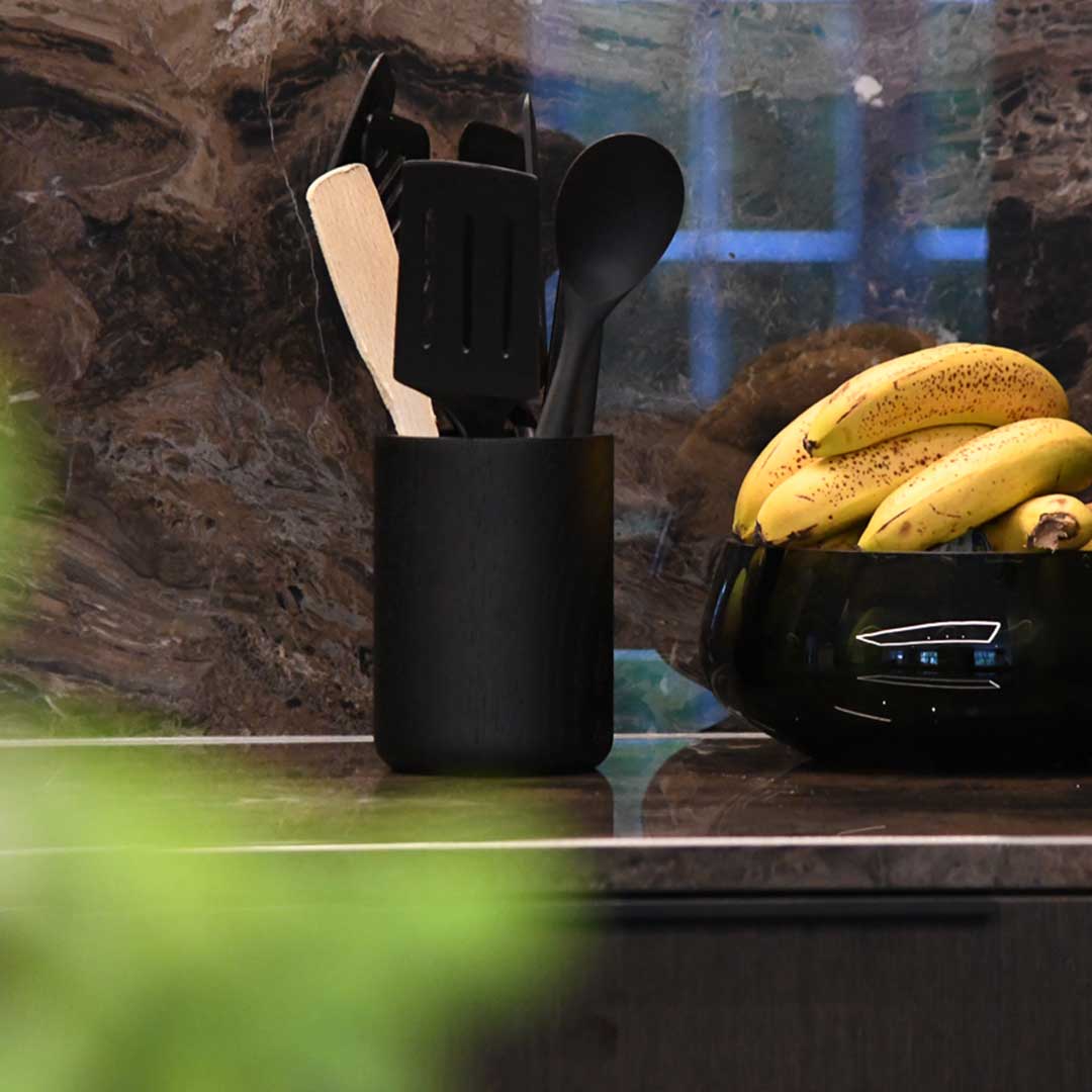 Küchenutensilienhalter aus Eichenholz schwarz, Milieubild in Küche, im Halter sind Holz und schwarze Küchenutensilien, rechts daneben sind Bananein in einer schwarzen Schüssel