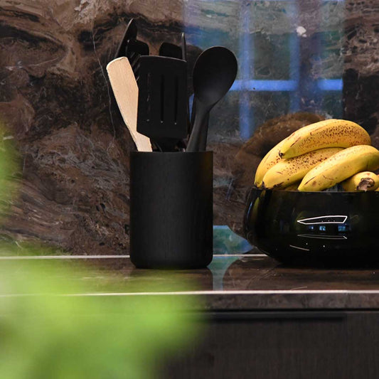 Küchenutensilienhalter aus Eichenholz schwarz, Milieubild in Küche, im Halter sind Holz und schwarze Küchenutensilien, rechts daneben sind Bananein in einer schwarzen Schüssel