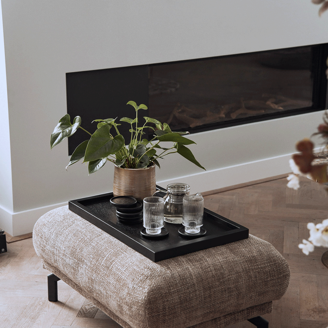 Serviertablett aus Eichenholz schwarz,40cm x 60cm, Ränder etwas höher, Milieubild im Wohnzimmer, Tablett steht auf Polsterhocker, Gläser und Pflanze stehen auf Serviertablett, Ansicht seitlich   