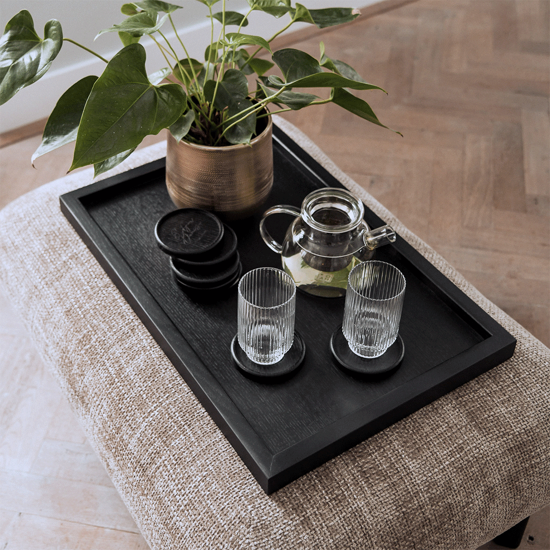 Serviertablett aus Eichenholz schwarz, 40cm x 60cm, Ränder etwas höher, Milieubild im Wohnzimmer, Tablett steht auf Polsterhocker, Gläser und Pflanze stehen auf Serviertablett, Ansicht von oben   