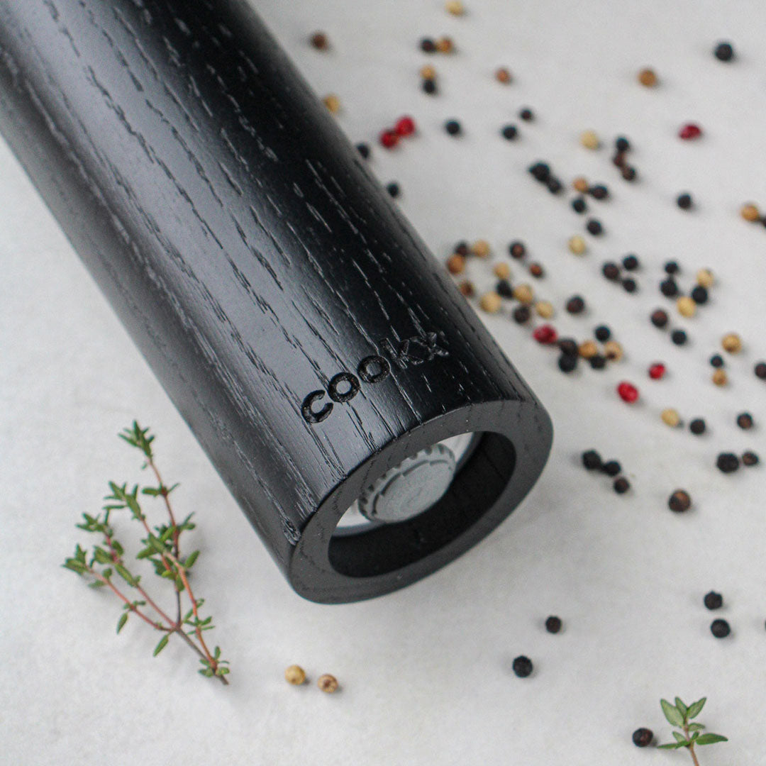 Salz-/Pfeffermühle aus Eichenholz schwarz, 23cm hoch, Milieubild, Pfeffermühle liegt auf Tisch, nur der untere Teil ist im Bild